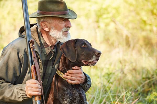 Mature man with gun and dog sit searching prey